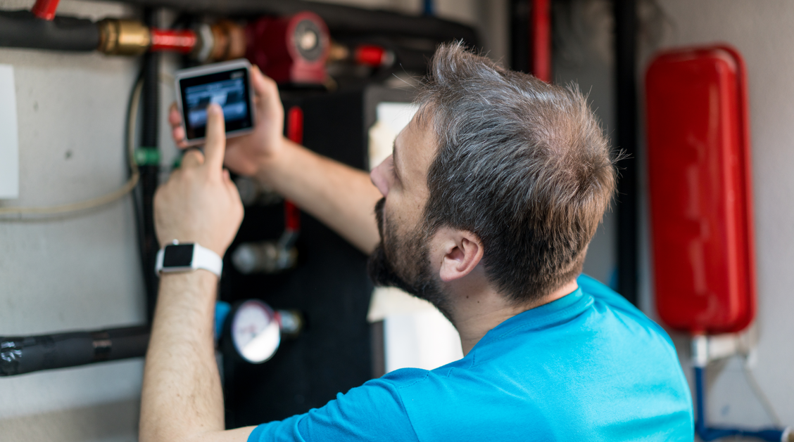 Ein Mann überprüft die Temperatur des Warmwasserbereiters mit einem Tablet. | © Getty Images