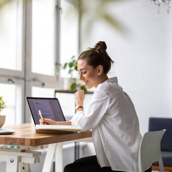 Eine Frau sitzt konzentriert an einem Schreibtisch, schaut auf ihren Laptop und arbeitet fleißig. | © Adobe Stock