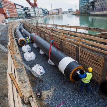 Ein Arbeiter in Sicherheitskleidung installiert eine Rohrleitung an einem Kanal. | © Peter Leßmann