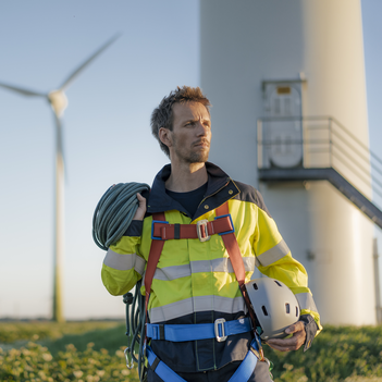 Ein Mann in Sicherheitsweste steht vor Windturbinen. Er überwacht die Anlagen, um sicherzustellen, dass sie einwandfrei funktionieren. | © Westend61 / Joseffson