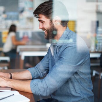 Ein Mann sitzt an einem Tisch an einem Laptop. Er arbeitet konzentriert und ist in seine Aufgaben vertieft. | © Getty Images