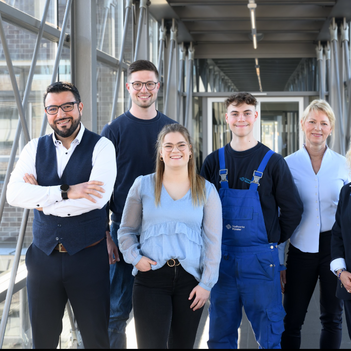 Sechs Mitarbeiter der Stadtnetze Münster stehen in einem verglasten Durchgang und lächeln. | © Stadtwerke Münster