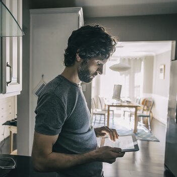 Ein Mann steht in der Küche und schaut auf sein Handy. | © Getty Images
